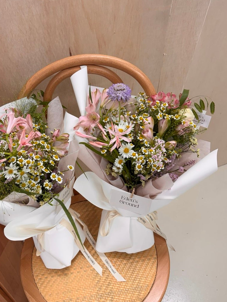 Pink flowers with daisy mix Bouquet, along with filler foliage, wrapped with pink tissue paper and white glassine paper, crafted by Eden's Ground, a floral design boutique.