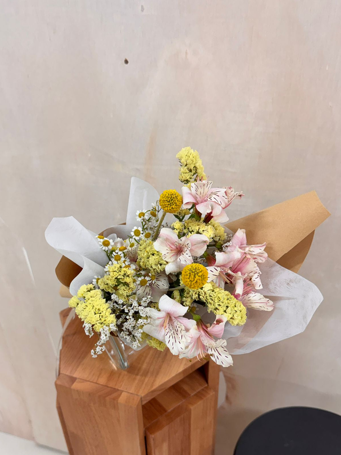 Pink flowers with daisy mix Bouquet, along with yellow filler foliage, wrapped with white tissue paper and brown kraft paper, crafted by Eden's Ground, a floral design boutique.