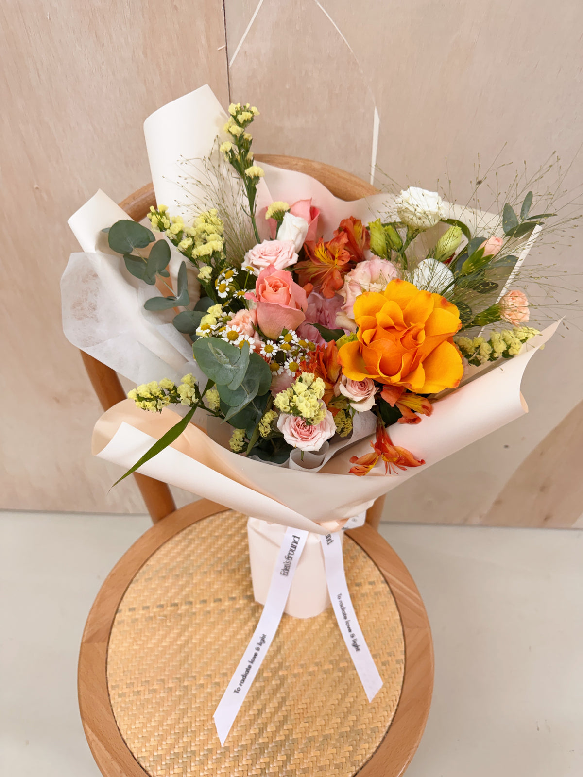 Pink flowers with daisy mix Bouquet, along with yellow filler foliage, wrapped with white tissue paper and brown kraft paper, crafted by Eden's Ground, a floral design boutique.