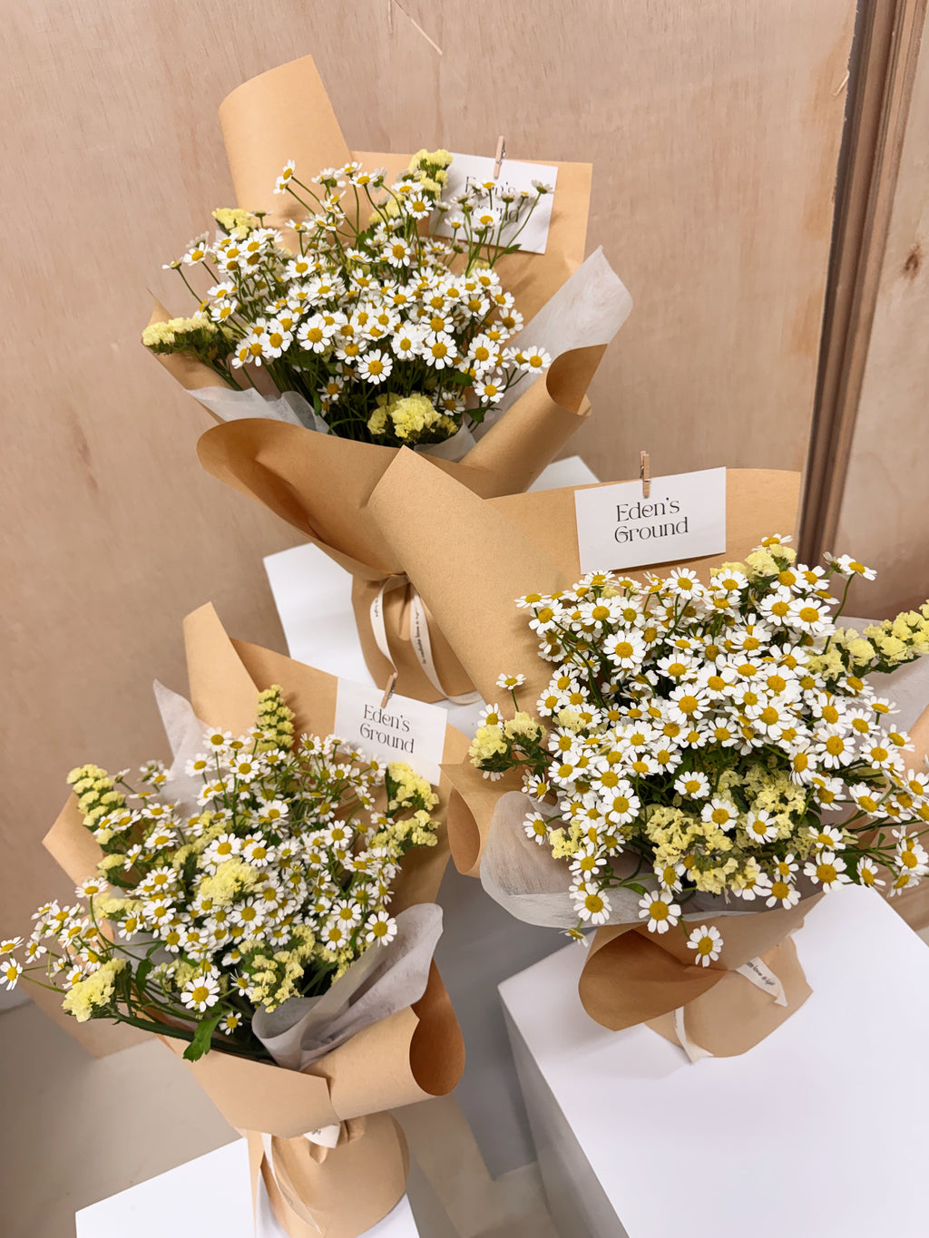 A bouquet of chamomile daisies, wrapped in brown kraft paper and sheer white tissue, crafted by Eden's Ground, a floral design studio in Singapore.