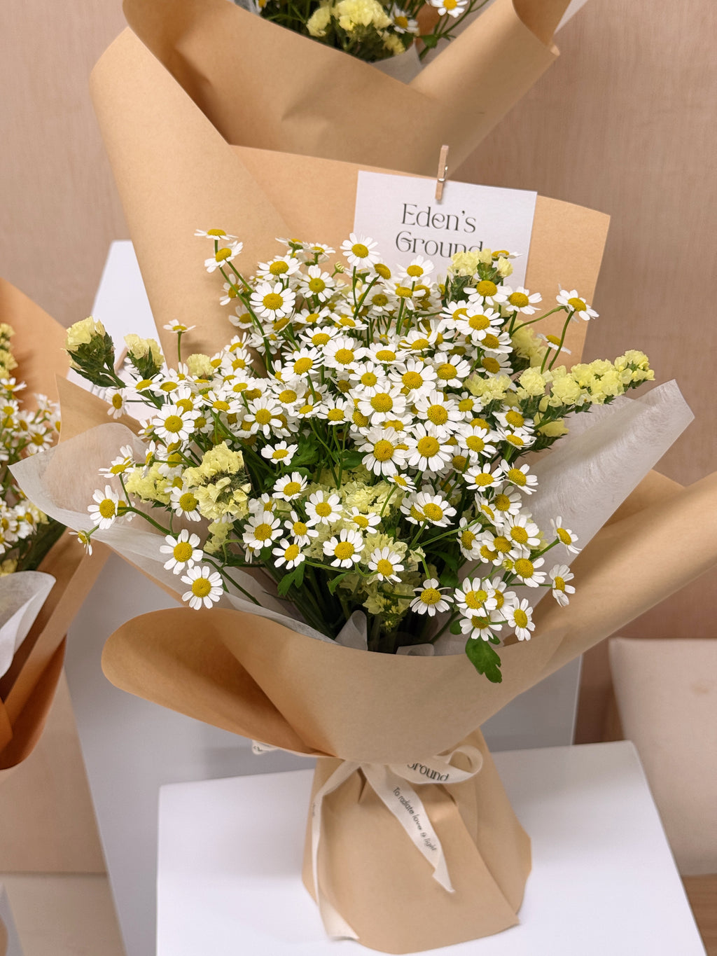 A bouquet of chamomile daisies, wrapped in brown kraft paper and sheer white tissue, crafted by Eden's Ground, a floral design studio in Singapore.
