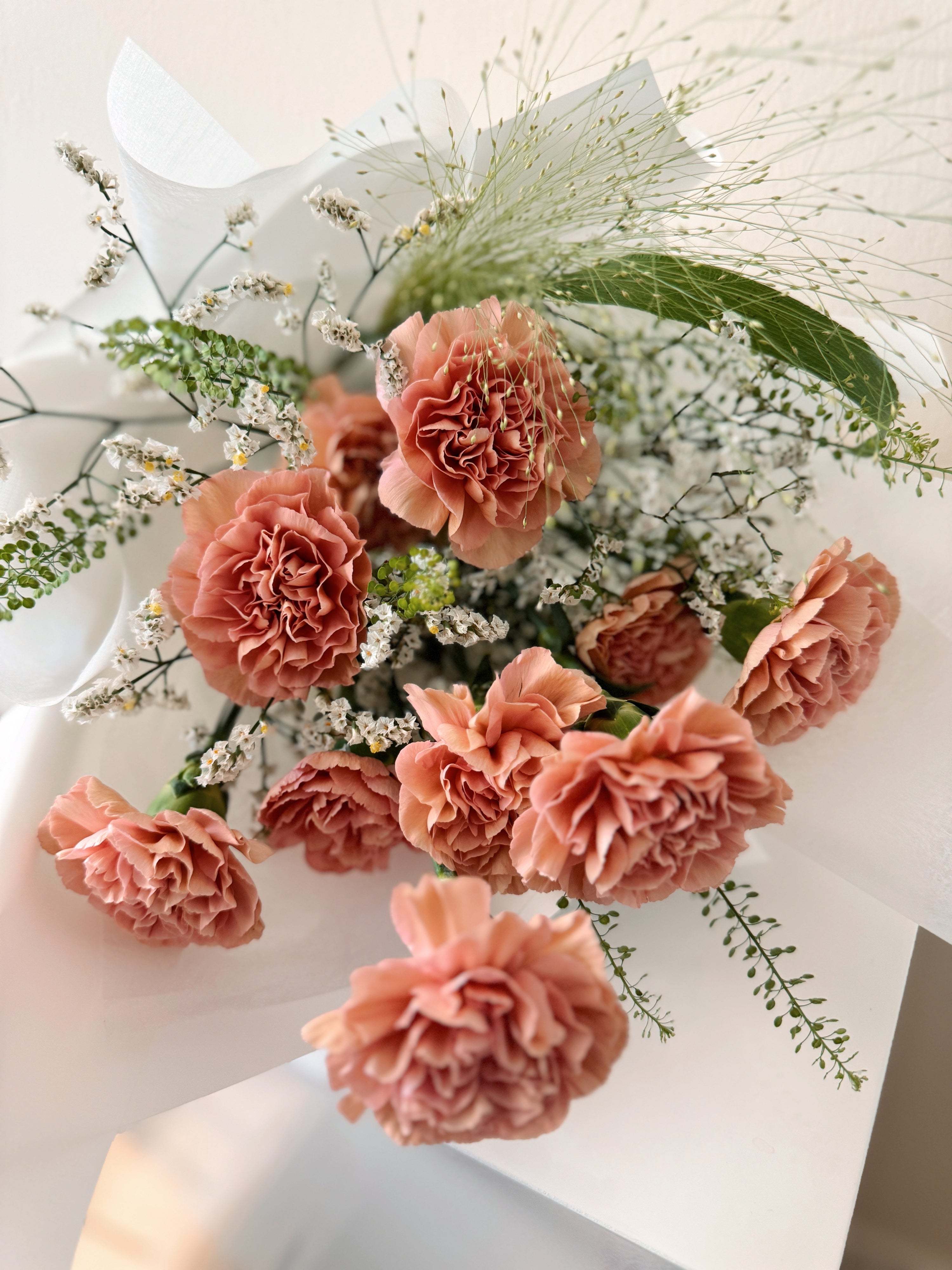 Grateful heart bouquet made with fresh carnations along with filler flowers and foliage, wrapped in tissue and white glassine paper crafted by Eden’s Ground.